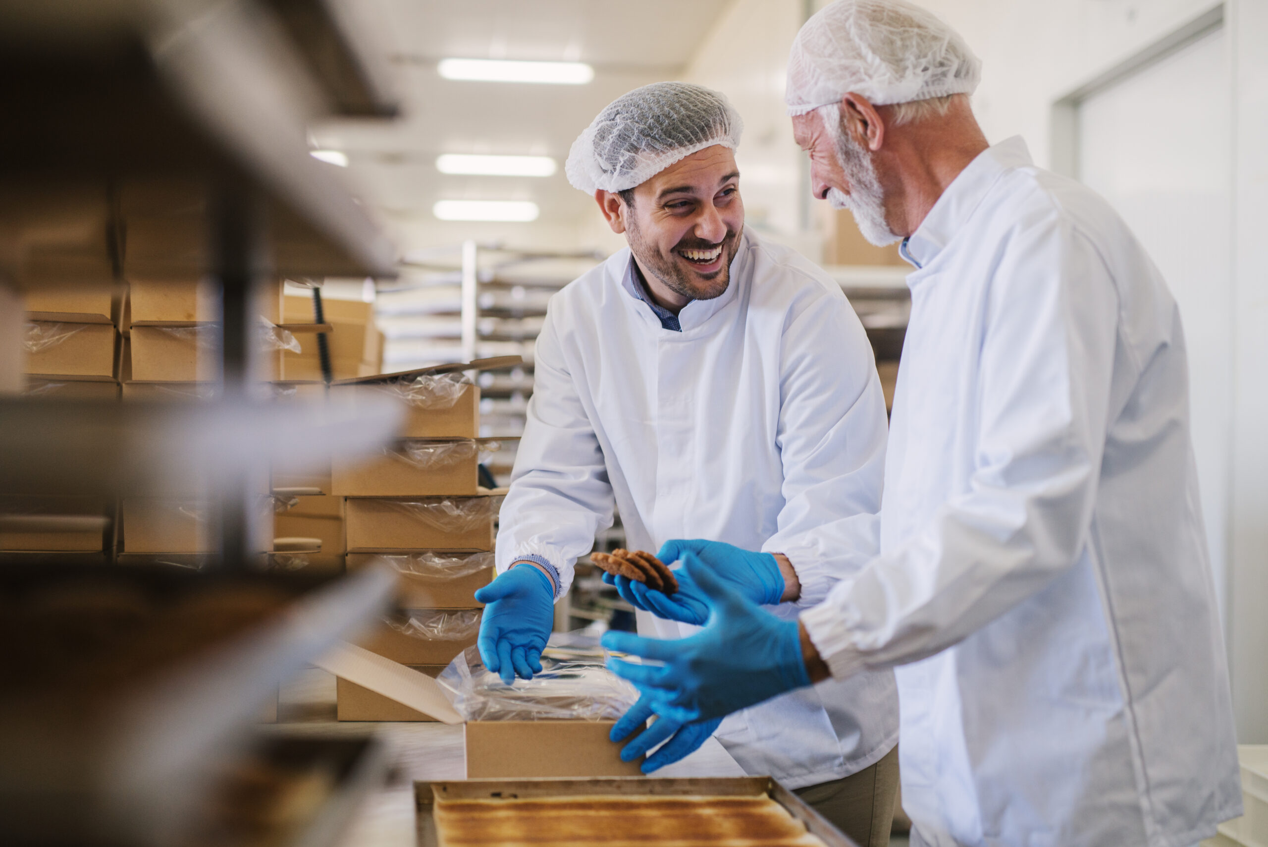 Picture of two male food factory employees in sterile clothes packing fresh made cookies and having fun